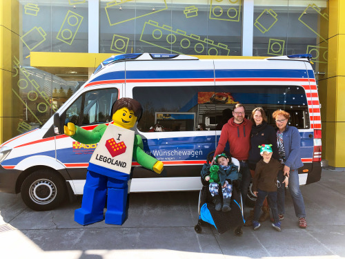 Parkmaskottchen LEGOLAND Boy begrüßt den Wünschewagen mit Jacob und seiner Familie am Parkeingang mit Freudensprüngen.